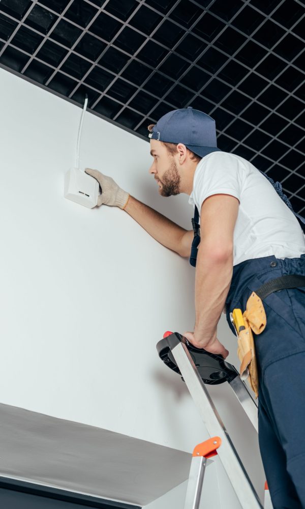 low angle view of young electrician fixing home alarm low angle view of young electrician fixing home alarm